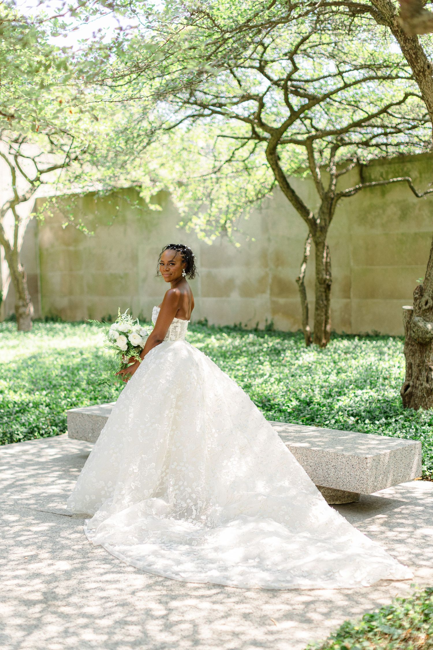 A stunning bridal portrait showcasing an elegant white gown with a flowing train in a garden.