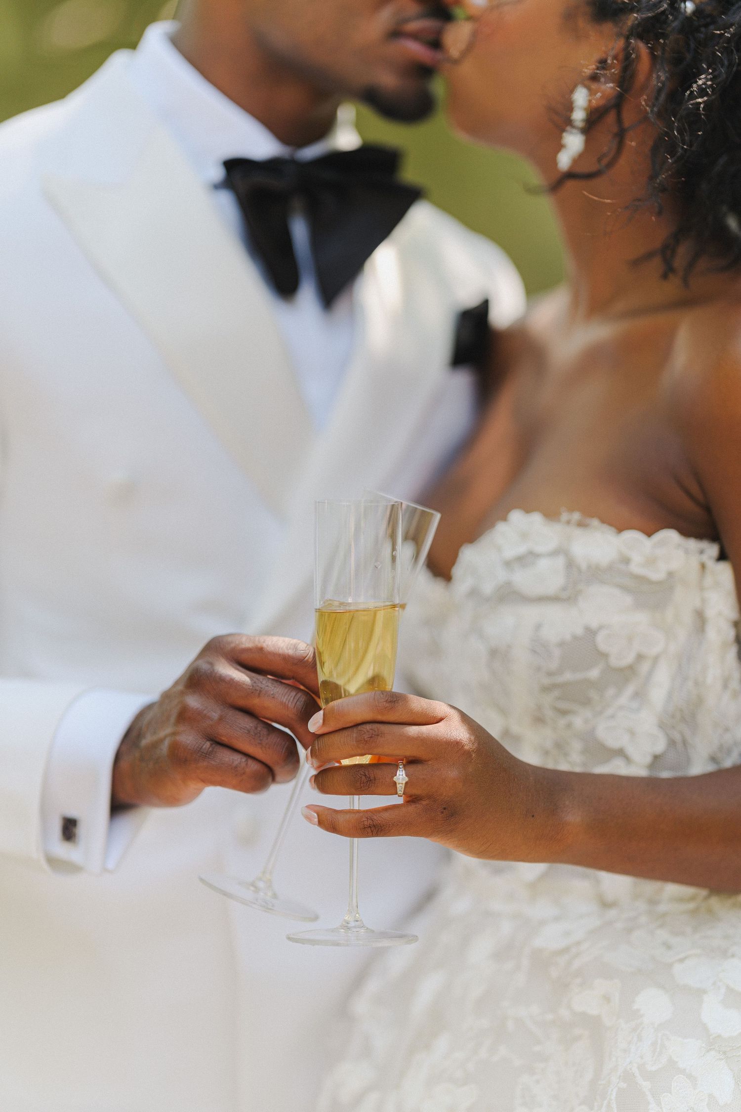 Close-up of champagne toast between newlyweds in formal attire.