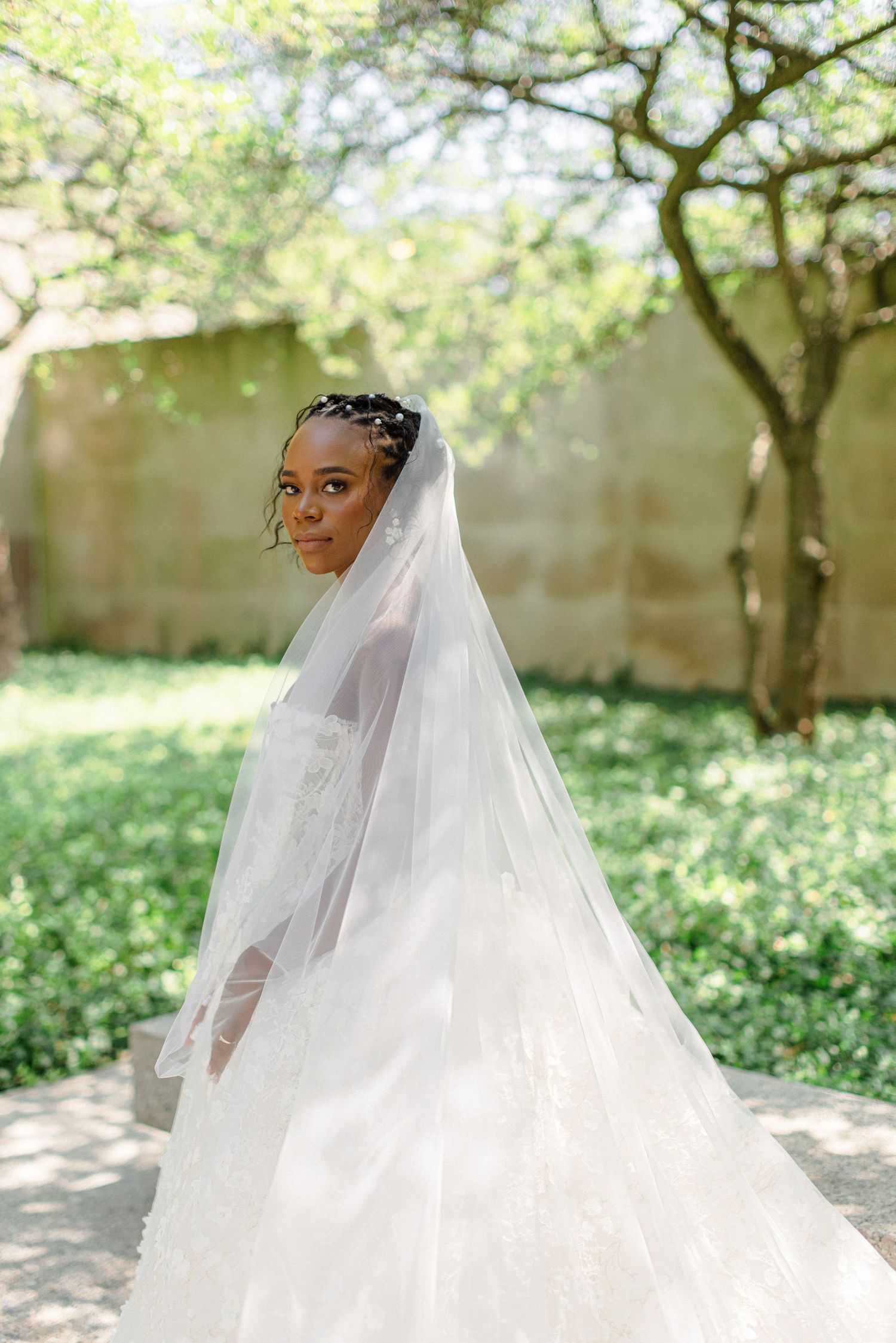 An elegant bridal portrait in a garden setting featuring a flowing white veil and gown.
