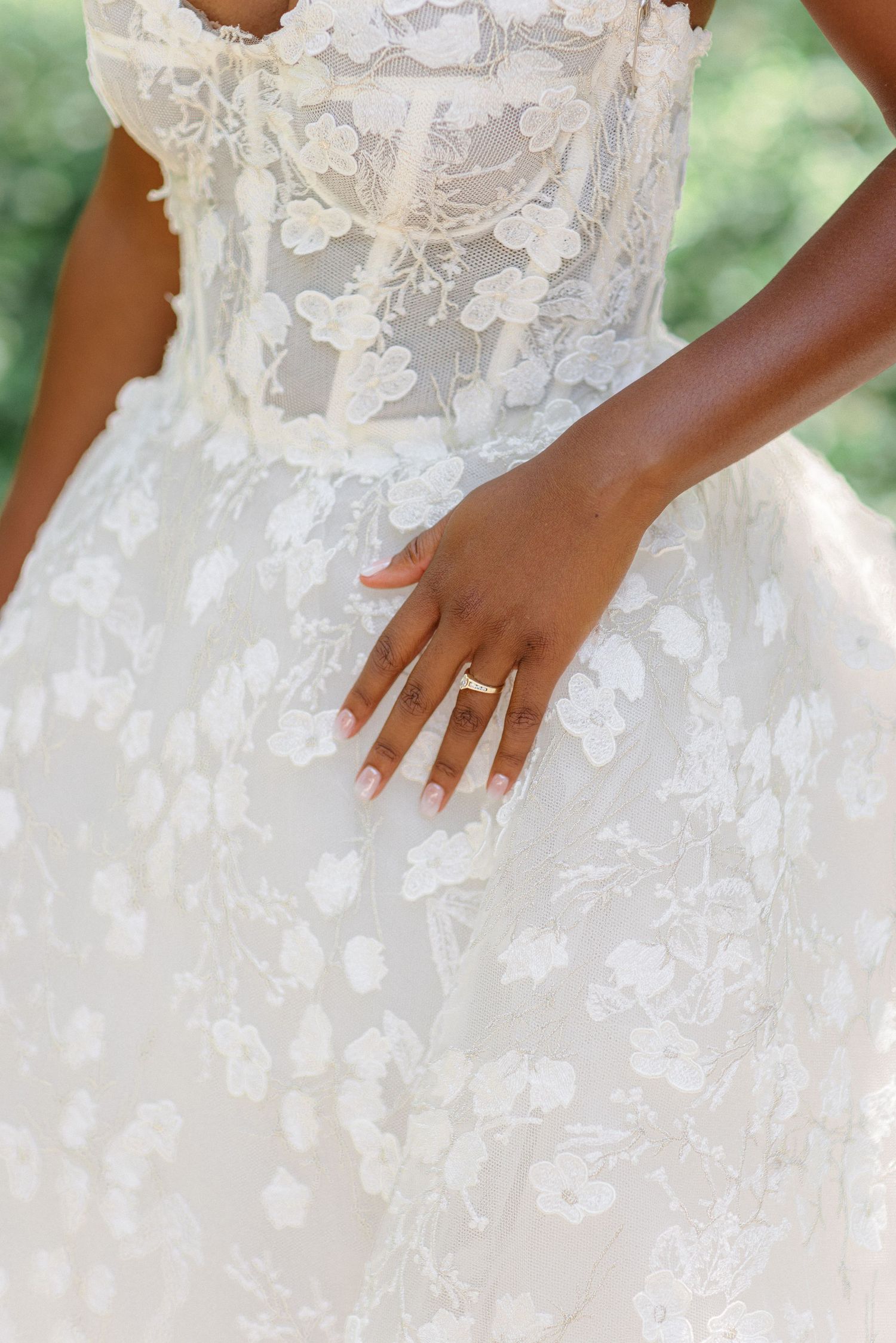 Close-up detail of an intricate lace wedding dress with a diamond ring on display.