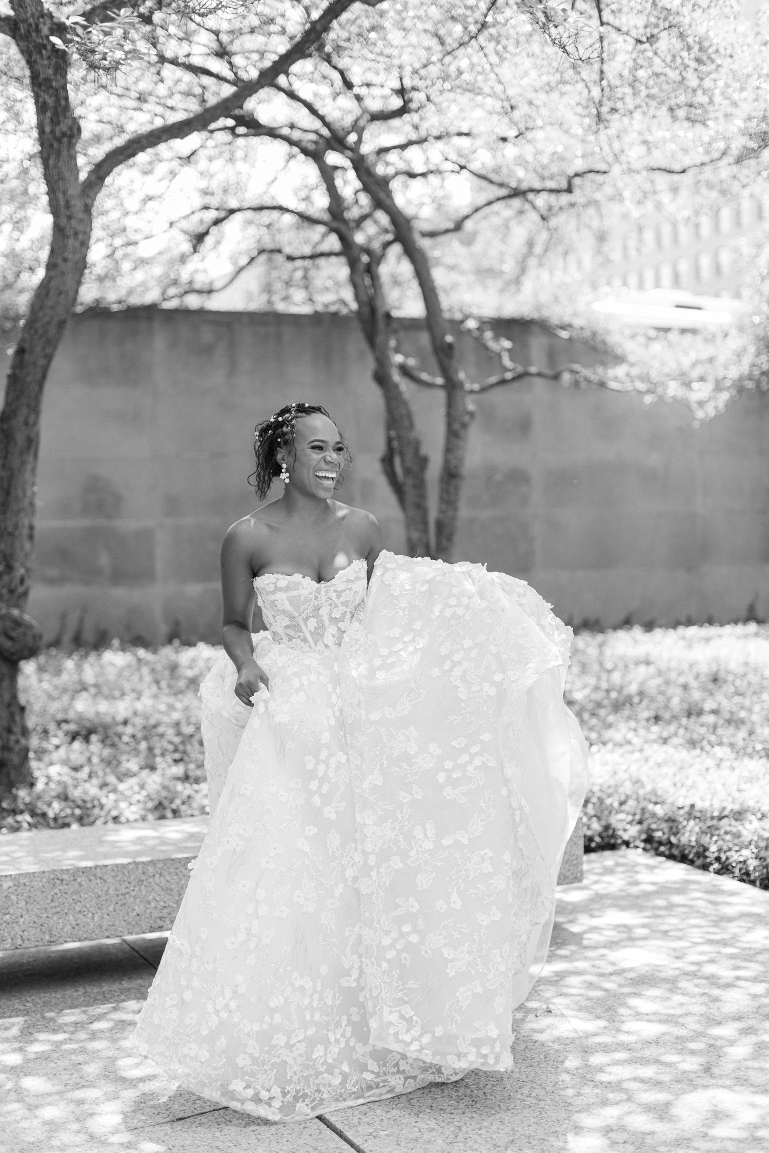 A black and white portrait of a bride in a detailed lace gown outdoors.
