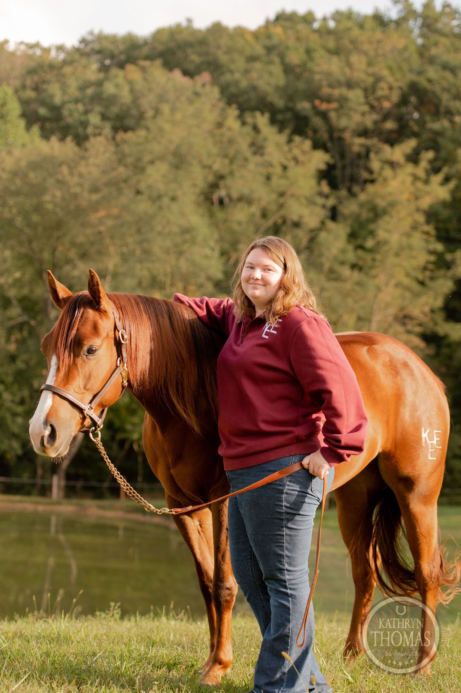 Beautiful chestnut horse and companion in maroon sweater pose in sunlit pasture.