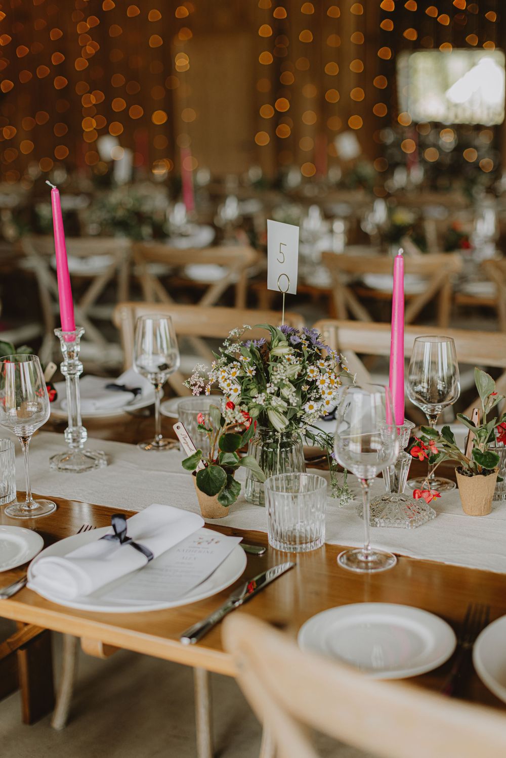 Elegant wedding table settings with pink straws, white plates, and floral centerpieces under warm lighting.