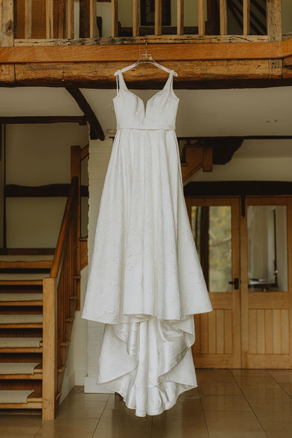 White wedding dress hanging on display against wooden beams in a rustic interior setting.