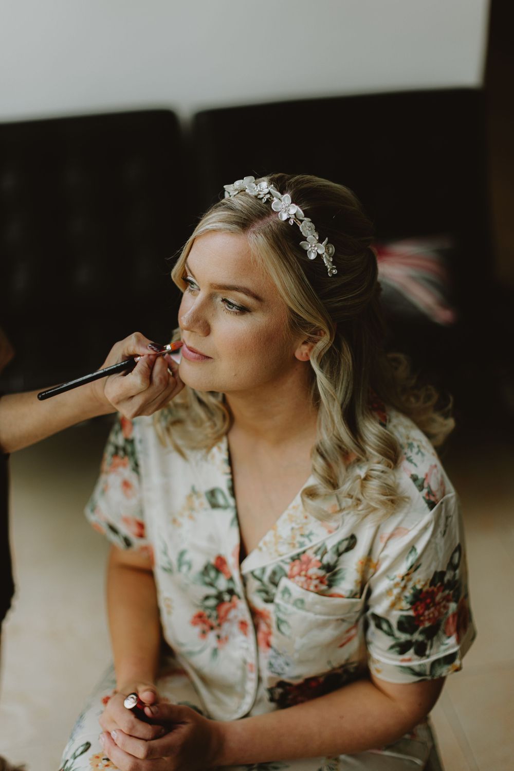 Someone getting makeup applied while wearing a floral robe during wedding preparations.