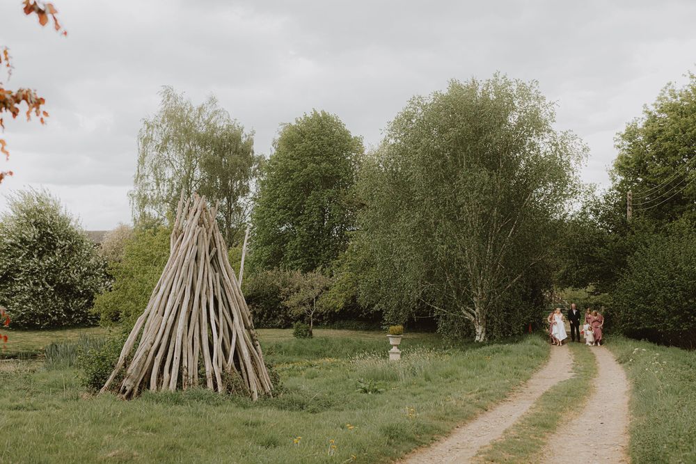 Wedding party walks along a scenic outdoor path lined with trees and greenery.