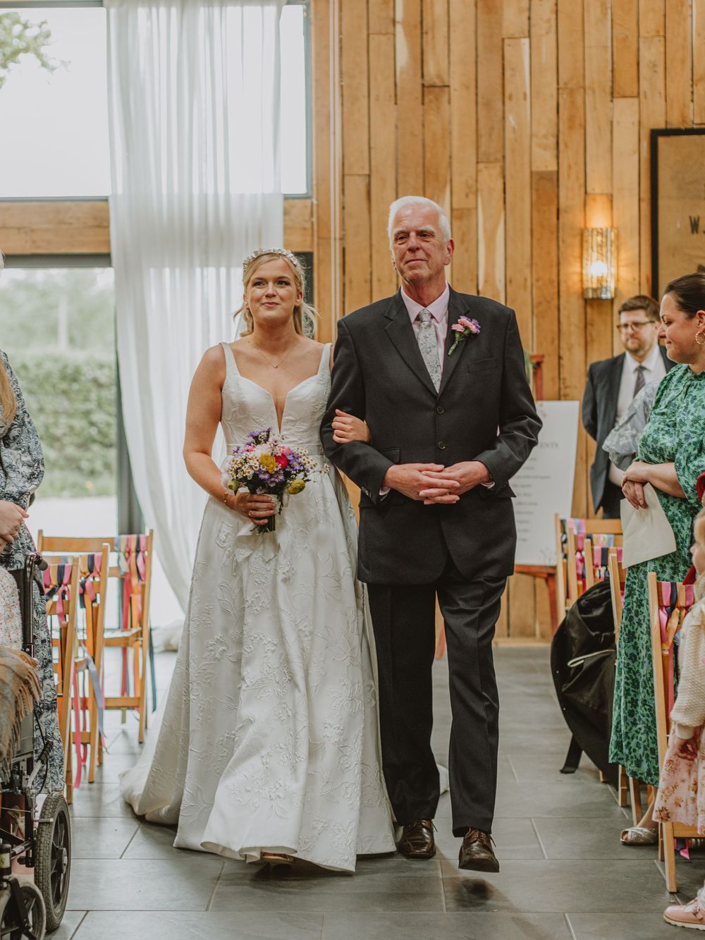 Wedding ceremony processional in a wooden paneled venue with natural lighting.