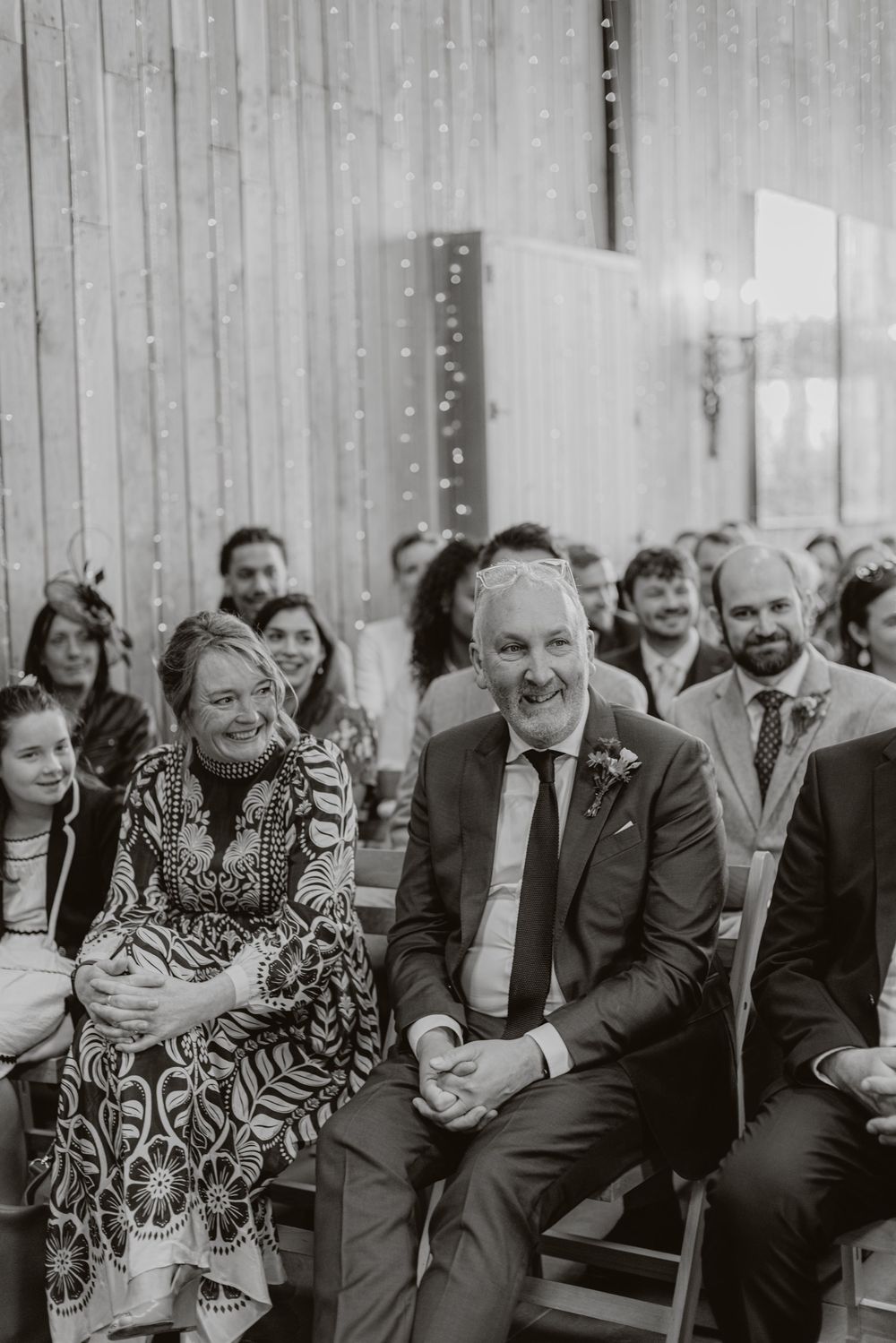 Wedding guests smile and laugh during an indoor ceremony.