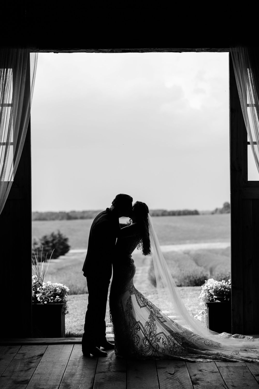 Romantic silhouette of newlyweds sharing an intimate moment in a rustic barn doorway with a scenic countryside backdrop.