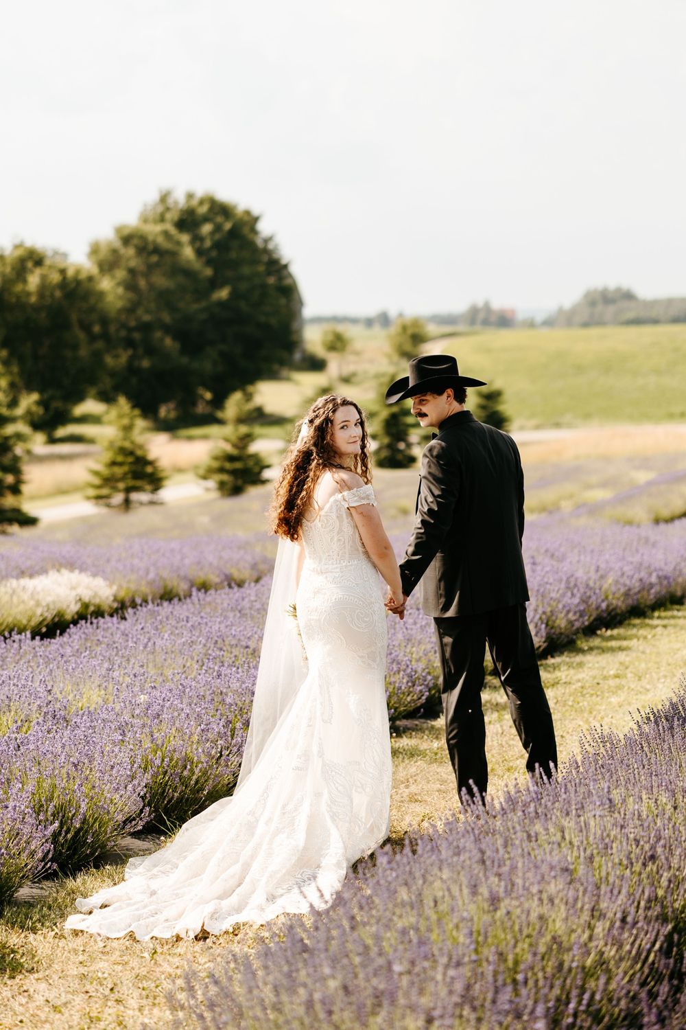 A couple poses together in a romantic field of blooming purple lavender flowers during their wedding day photo shoot.