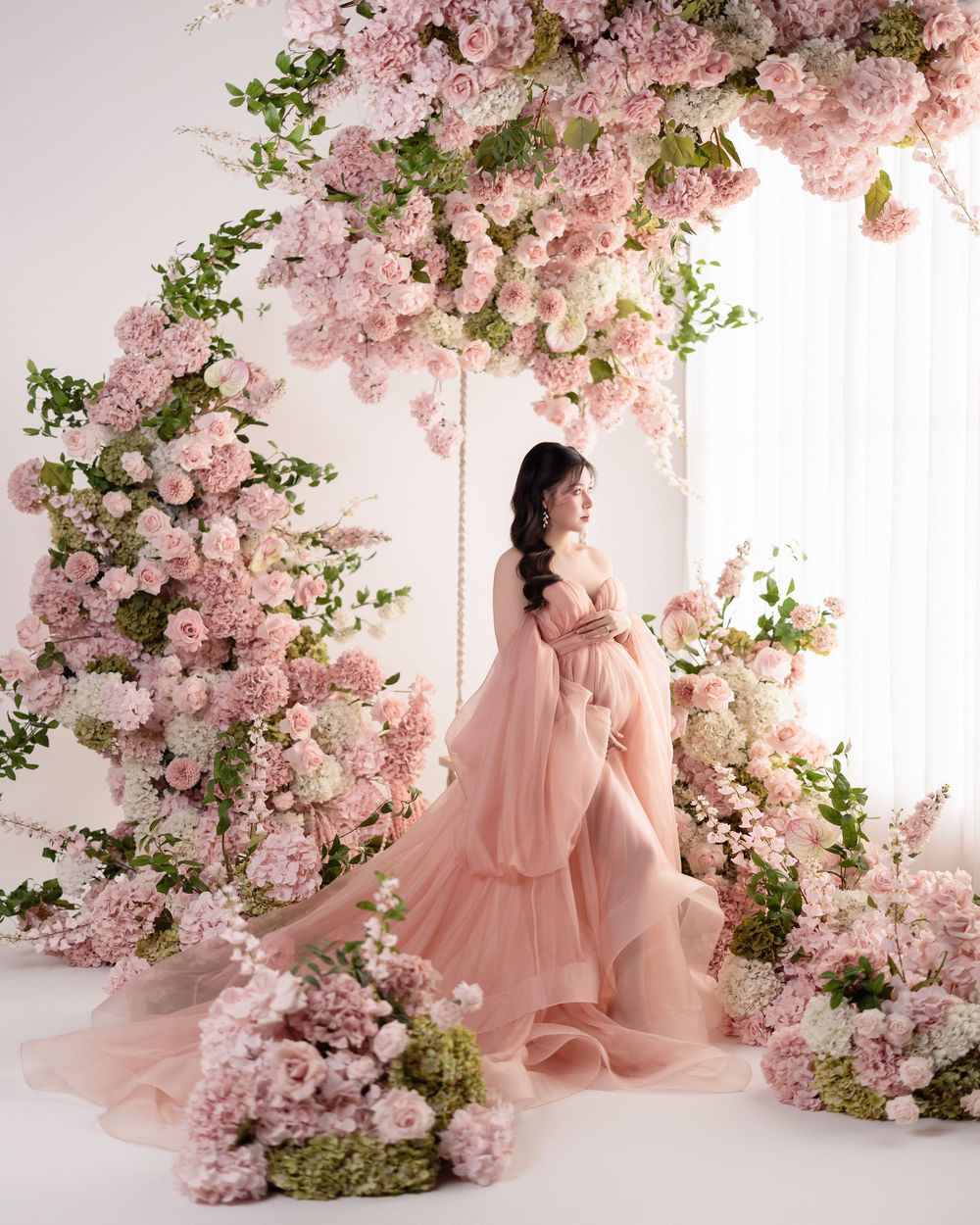 A dreamy portrait session with pink cherry blossoms and soft peach tulle dress against a light backdrop.