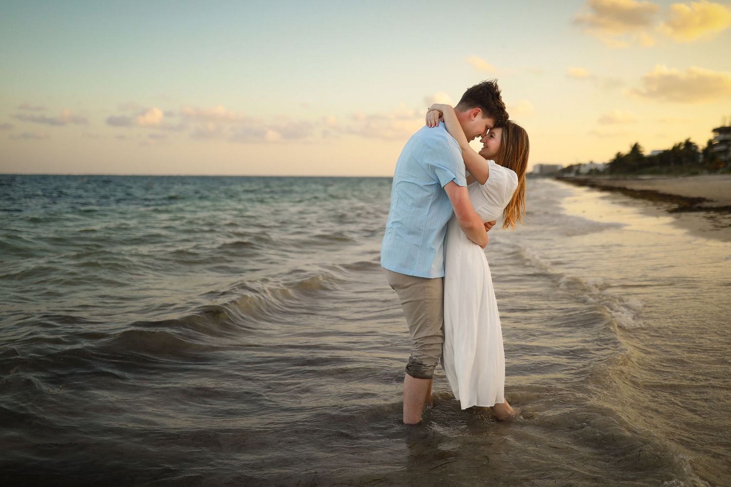 Romantic couple embracing at sunset on beach with waves lapping at their feet.