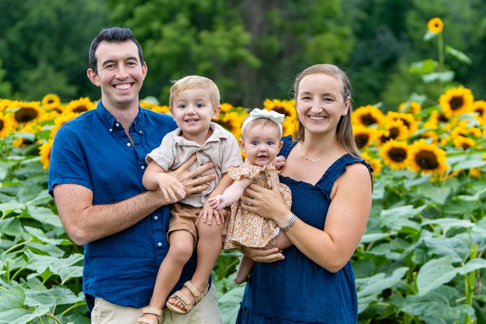 A family poses together during a family portrait photo session in a sunflower field at Verrill Farm in Concord, MA by Lisa West Photography.