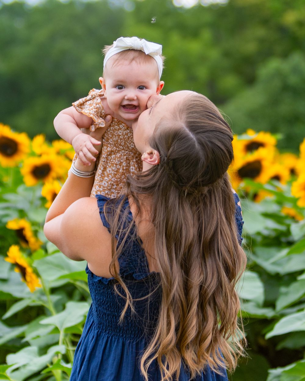 Mom & baby pose together during a family portrait photo session in a sunflower field- Verrill Farm in Concord, MA by Lisa West Photography.