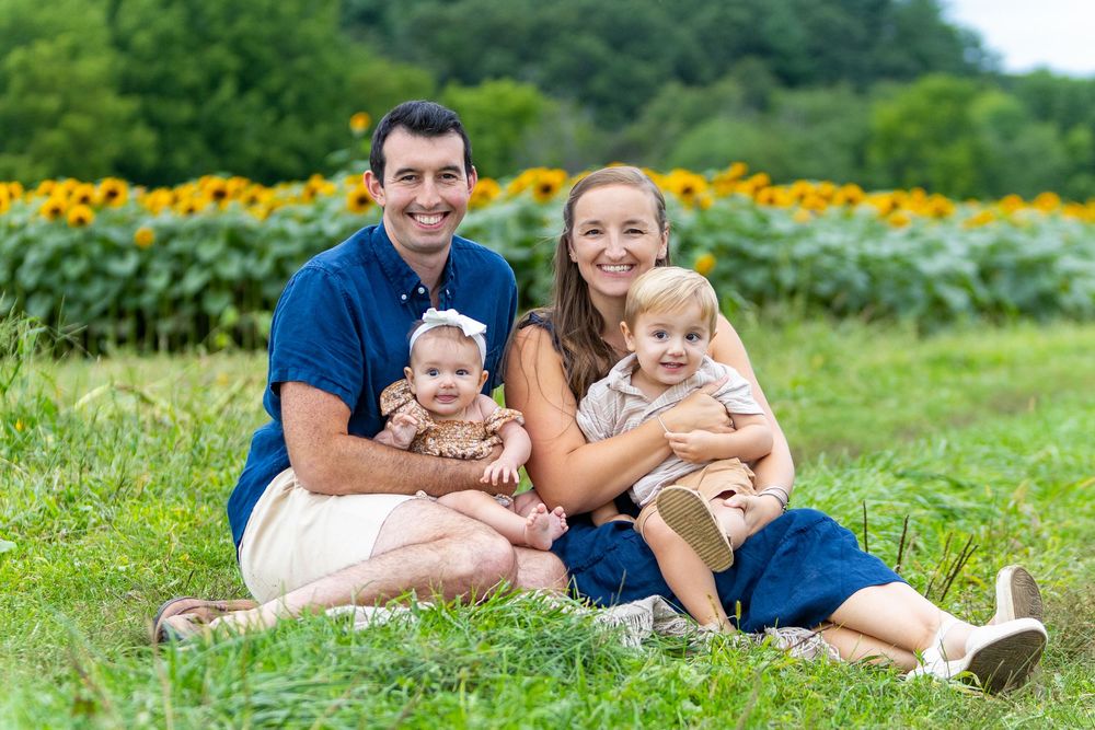 A family poses together during a family portrait photo session in a sunflower field at Verrill Farm in Concord, MA by Lisa West Photography.