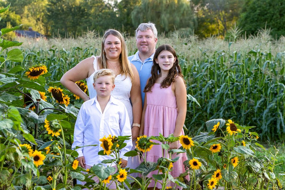 A family poses together during a family portrait photo session in a sunflower field at Verrill Farm in Concord, MA by Lisa West Photography.
