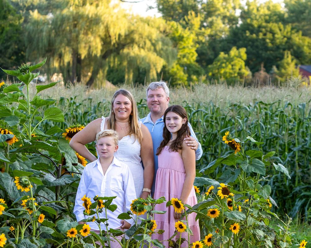 A family poses together during a family portrait photo session in a sunflower field at Verrill Farm in Concord, MA by Lisa West Photography.