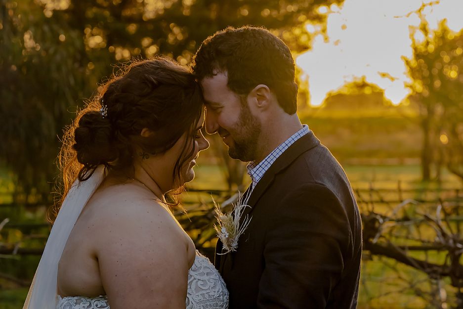 Lovers embrace in silhouette against a warm golden sunset with rustic wooden fences and glowing natural backlighting.