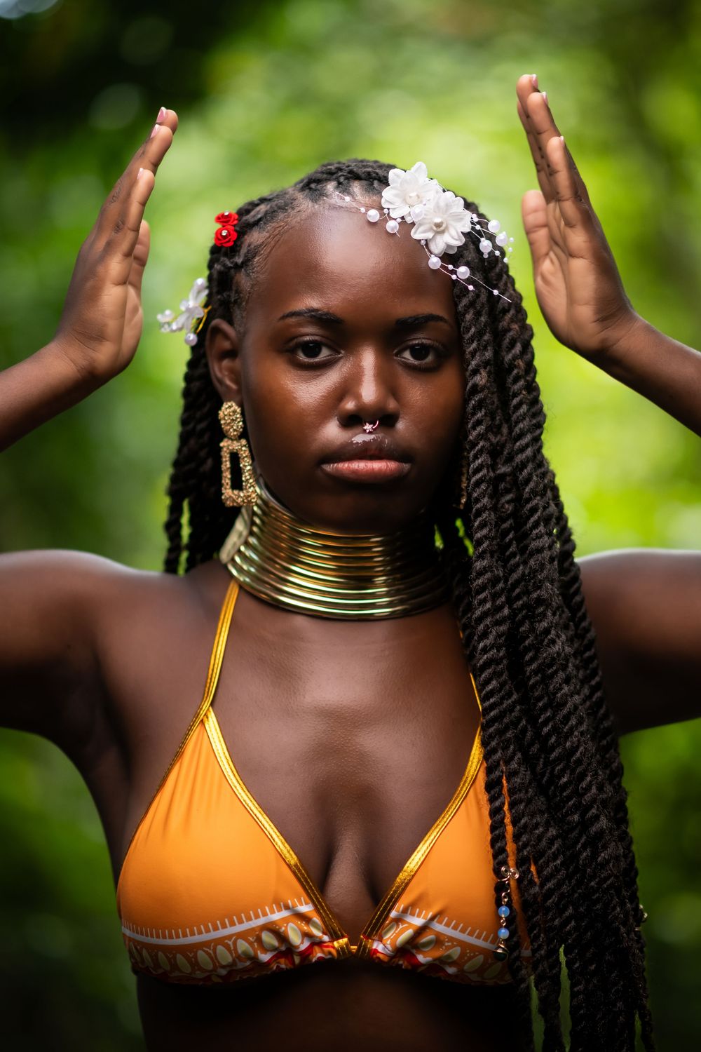 Striking portrait with traditional African neck rings, braided hair, and floral accessories against green backdrop.