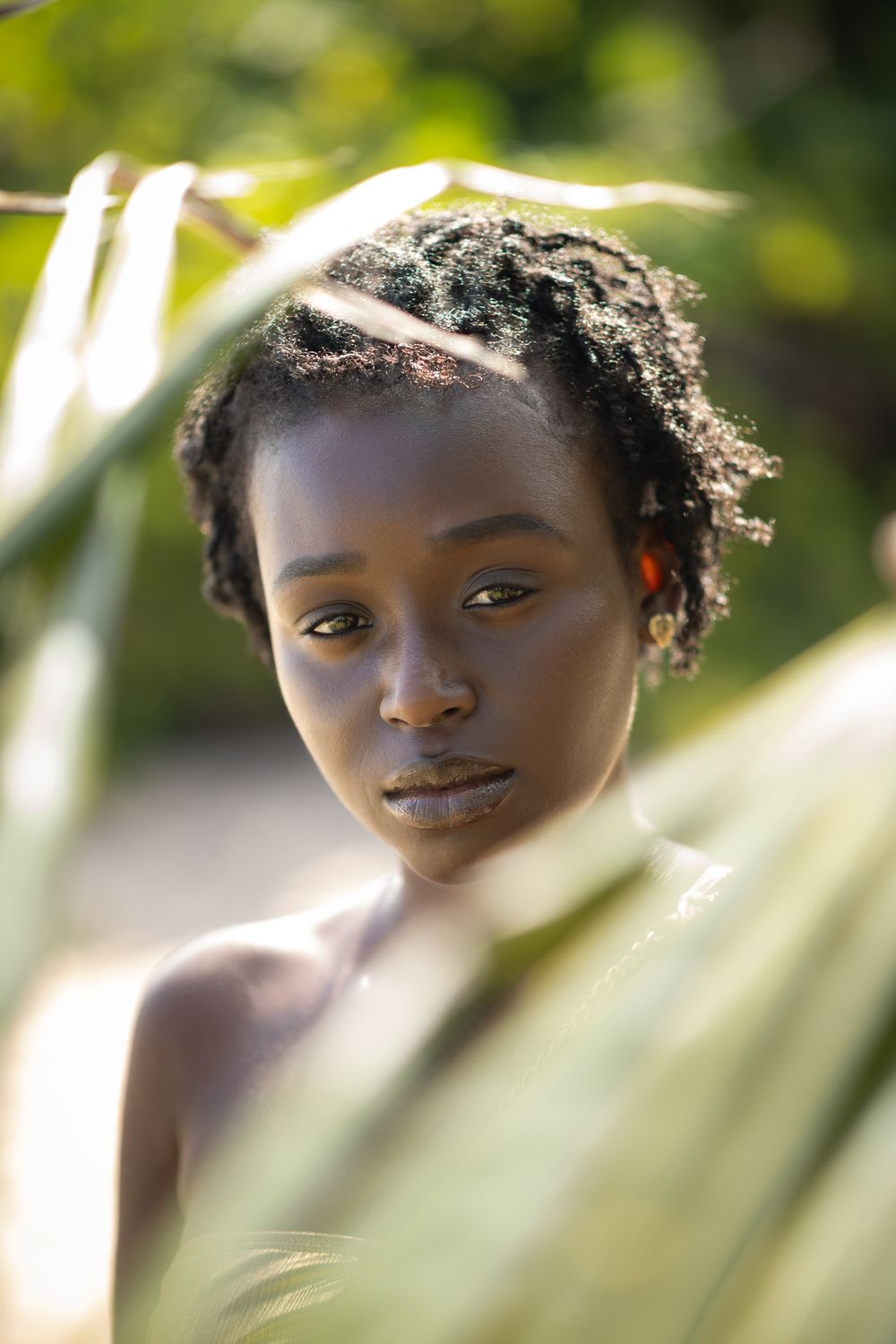 Soft-focus beauty portrait through palm leaves with natural lighting and minimalist styling.