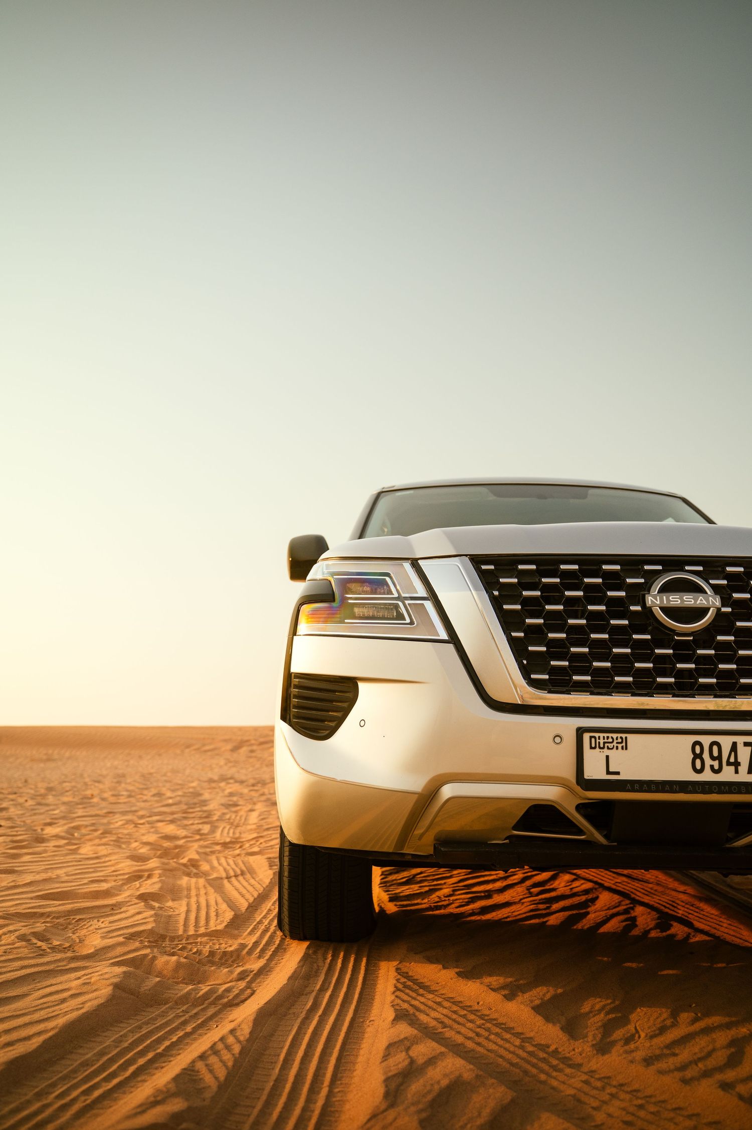 Nissan SUV with distinctive grille parked on desert sand dunes during golden hour lighting.