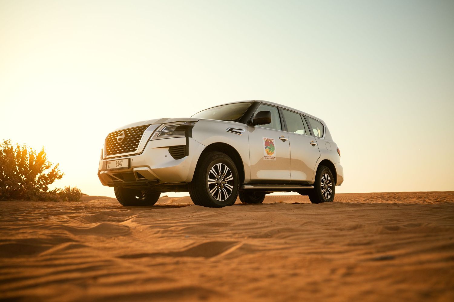 SUV cast in warm light during golden hour creates dramatic silhouettes against desert sand dunes.