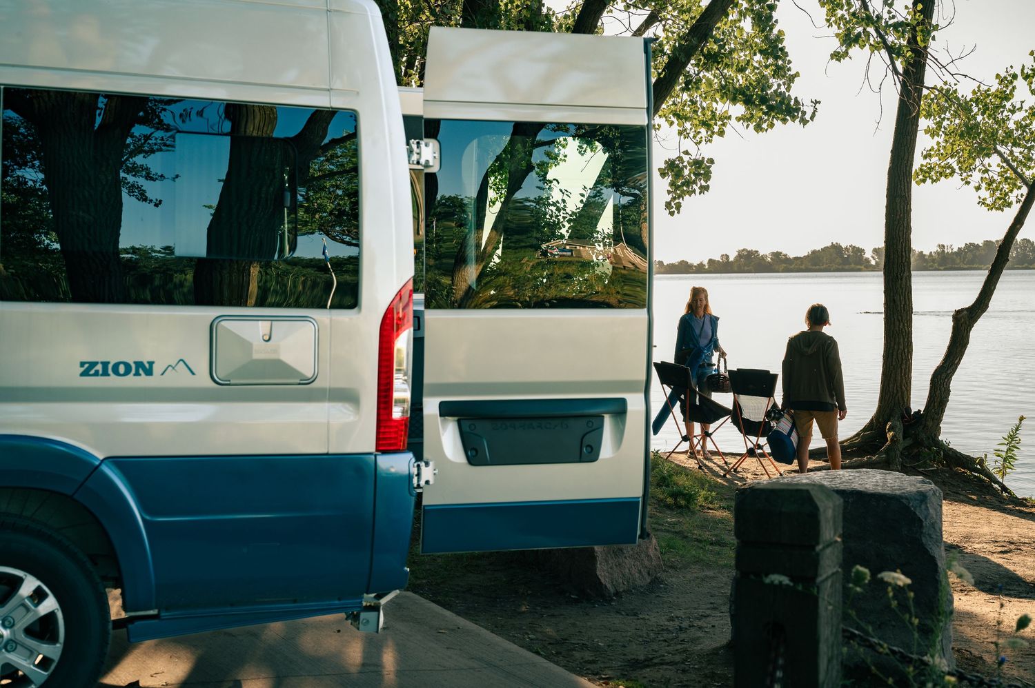 Van parked near lake shore with outdoor scene showing people sitting by water's edge in natural setting.