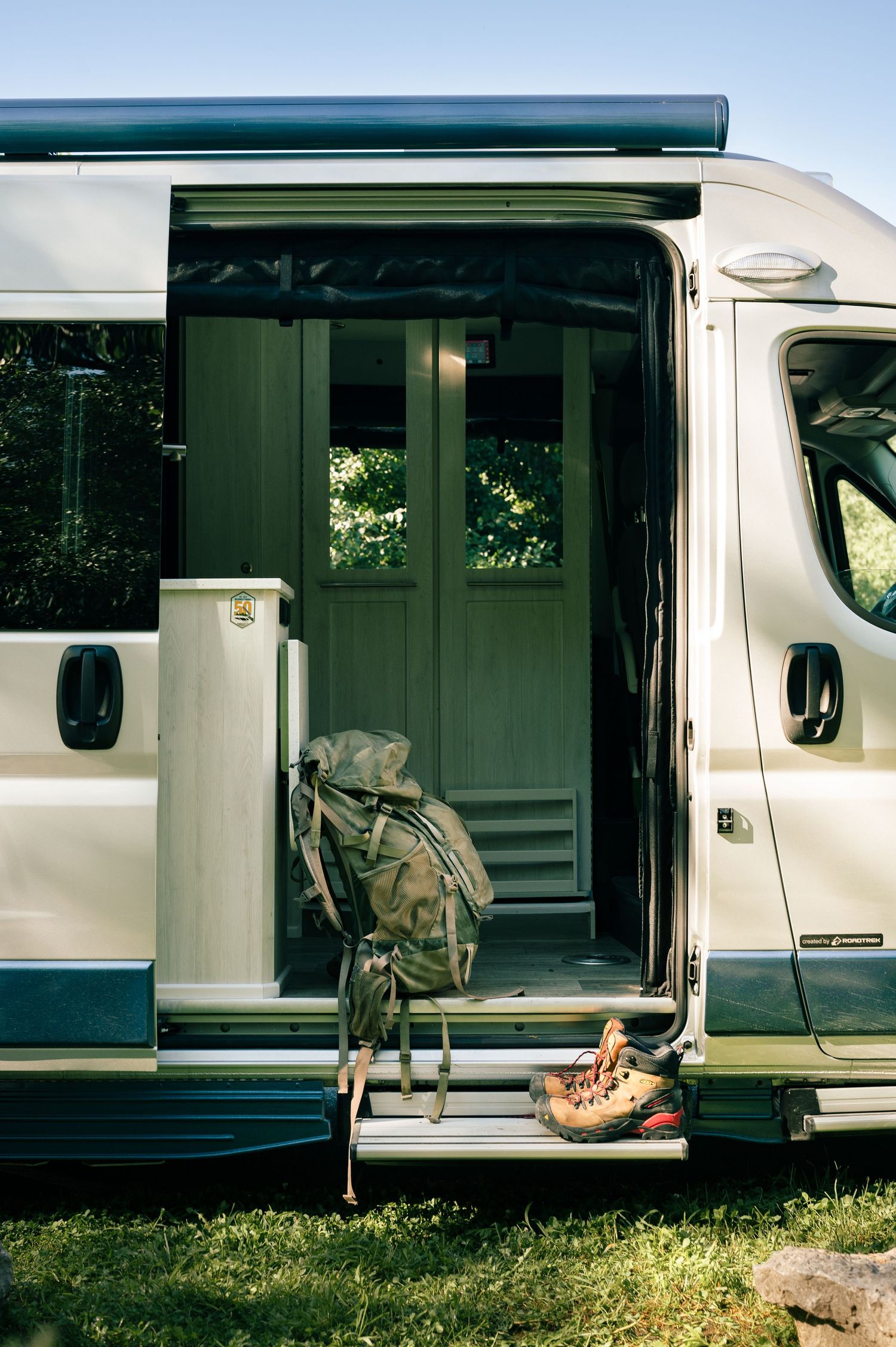 Side view of a white RV camper parked on grass with open sliding doors showing interior details.