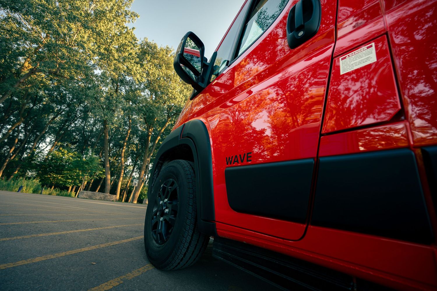 Low angle view of a bright red off-road vehicle's wheel and side panel parked on a tree-lined street.