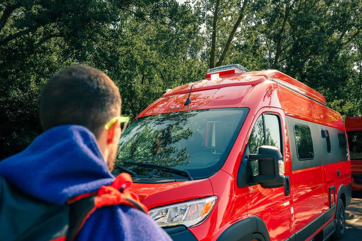 A bright red emergency response vehicle parked on a wooded road with someone in the foreground wearing blue.