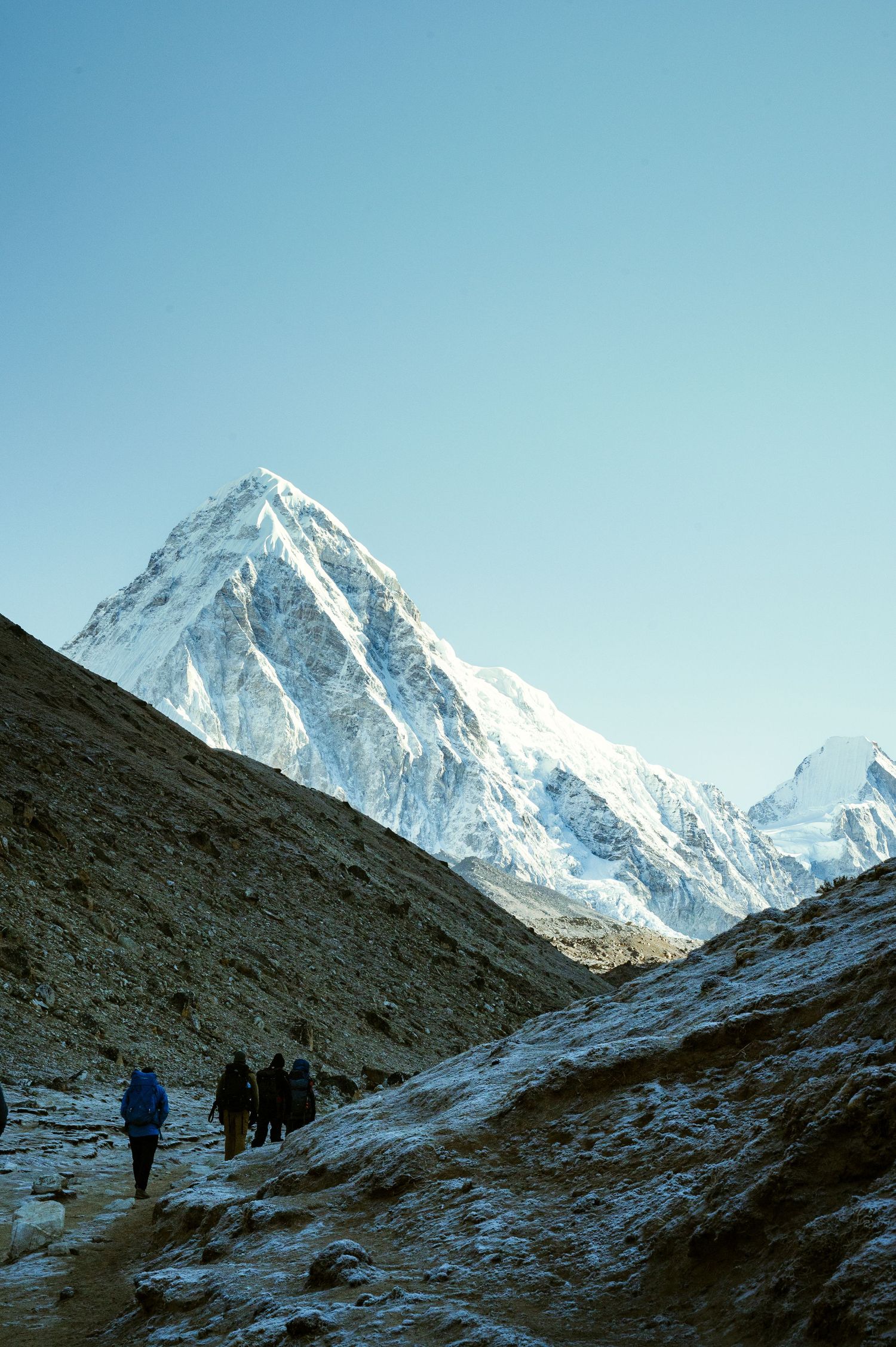 Snow-capped mountain peaks tower above trekking path in the Himalayas during winter.
