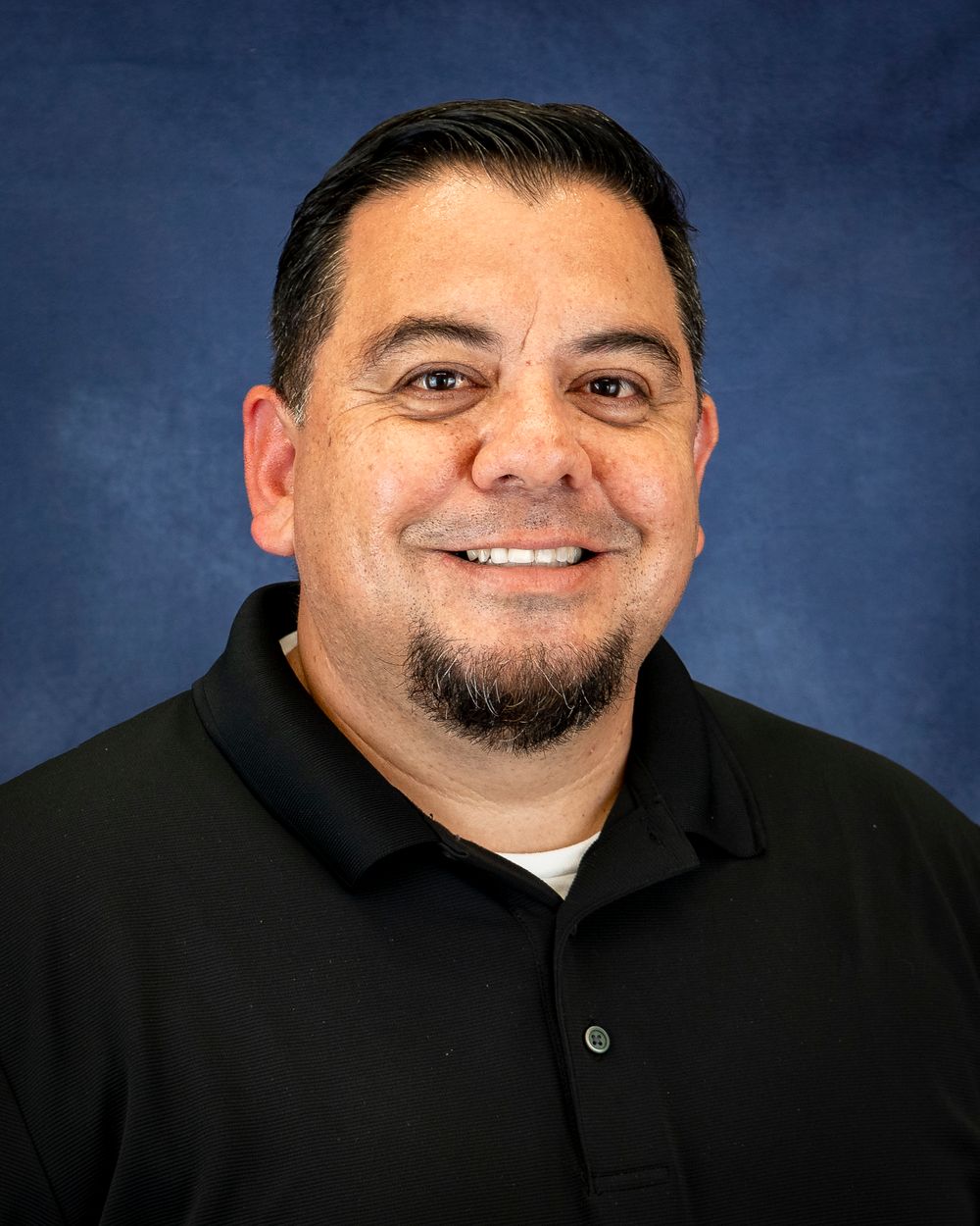 Portrait of a person in a black collared shirt against a blue studio backdrop.