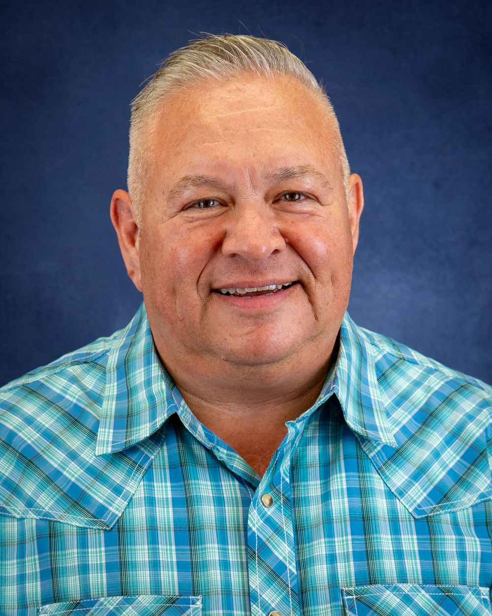 Portrait of a person in a teal plaid button-up shirt against a blue backdrop.
