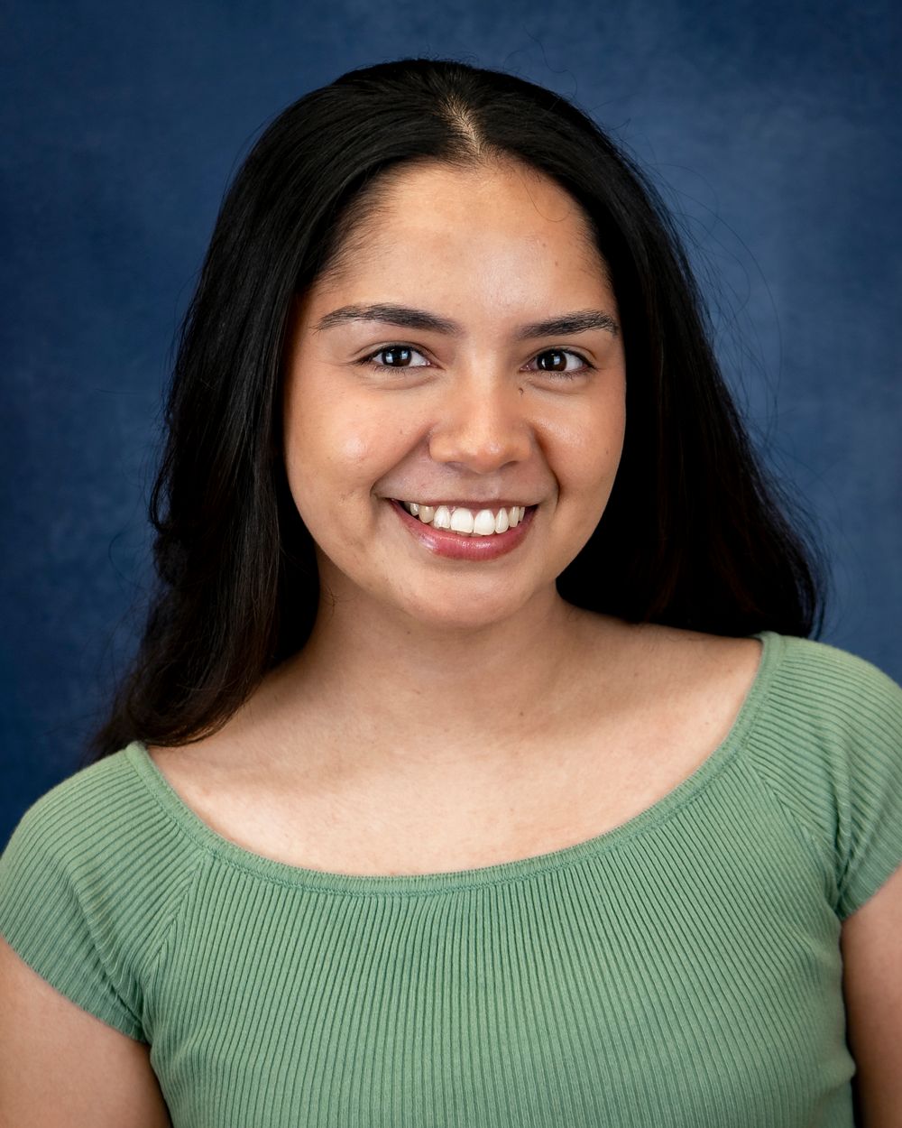 Portrait of a person wearing a light green ribbed top against a blue studio background.