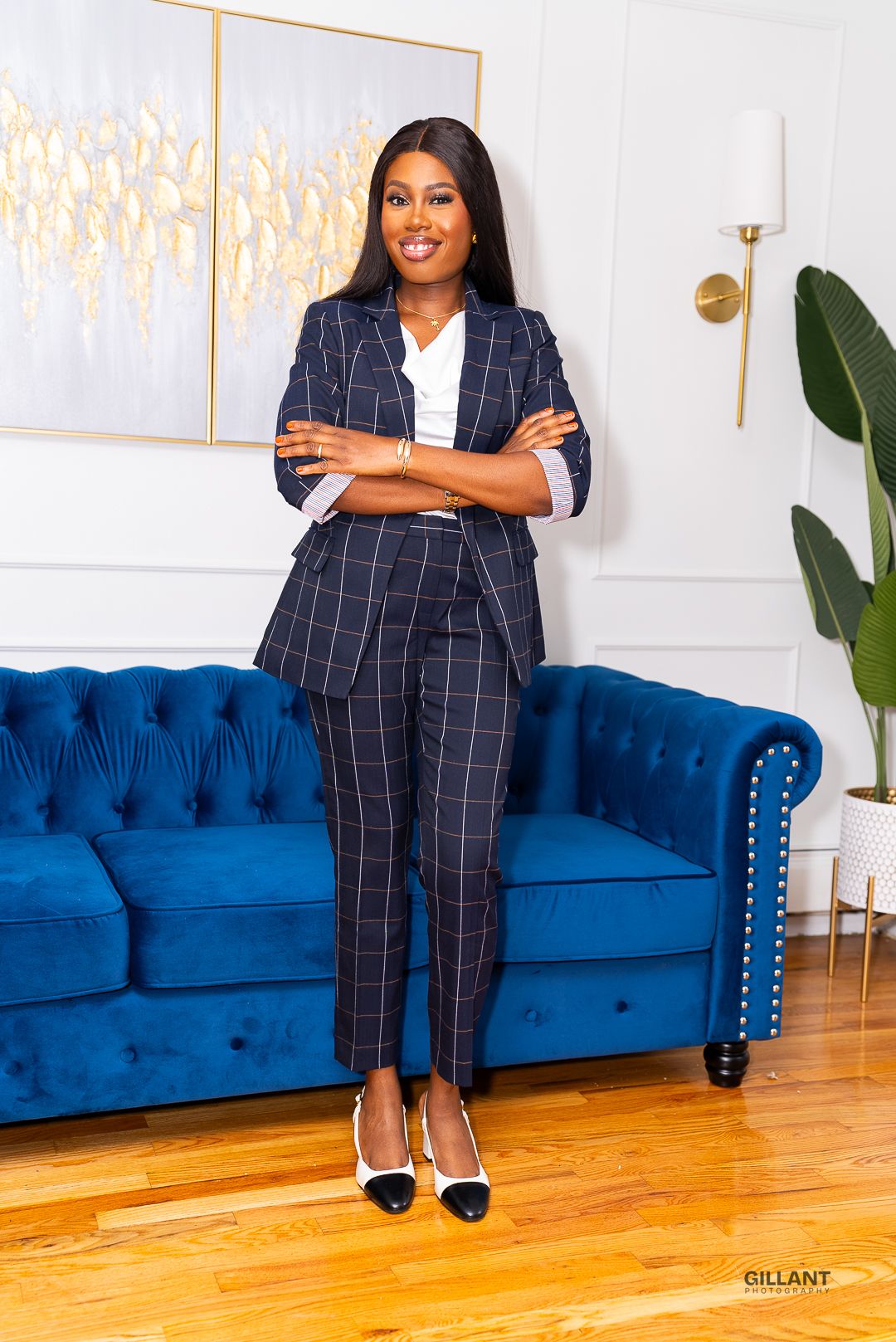 Business professional in navy pinstripe suit poses against blue velvet couch and modern decor.