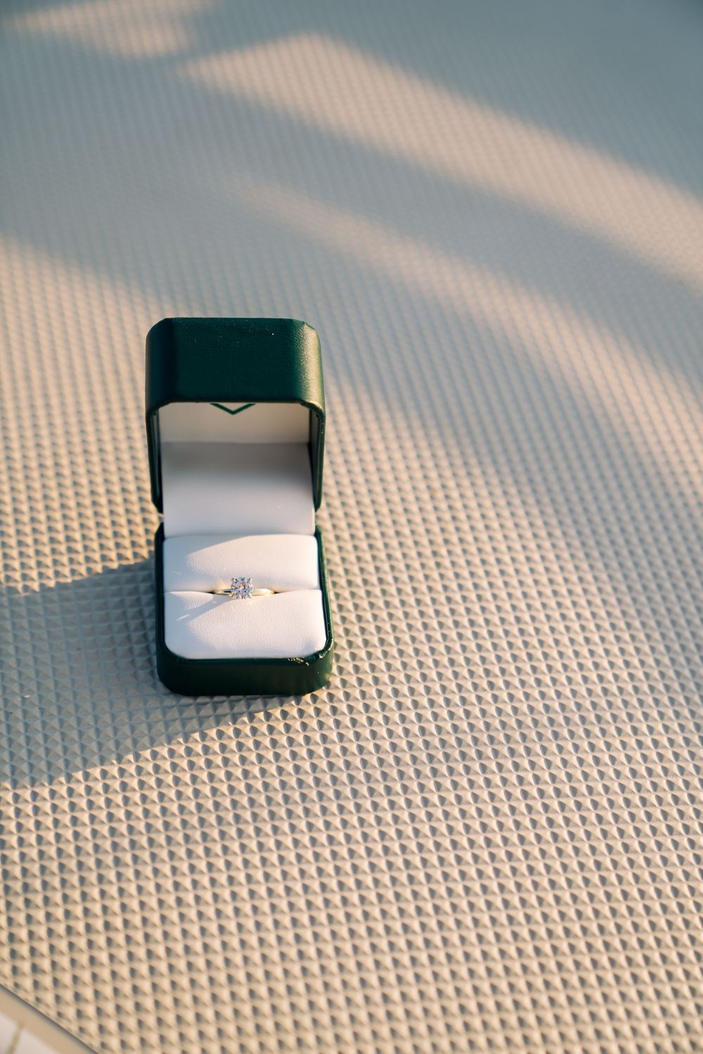 Diamond engagement ring in black velvet box sitting on textured white fabric.
