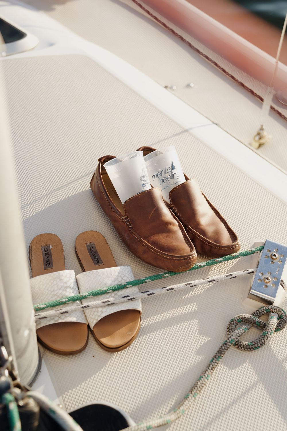 Brown leather loafers and sandals arranged on a white boat deck surface.