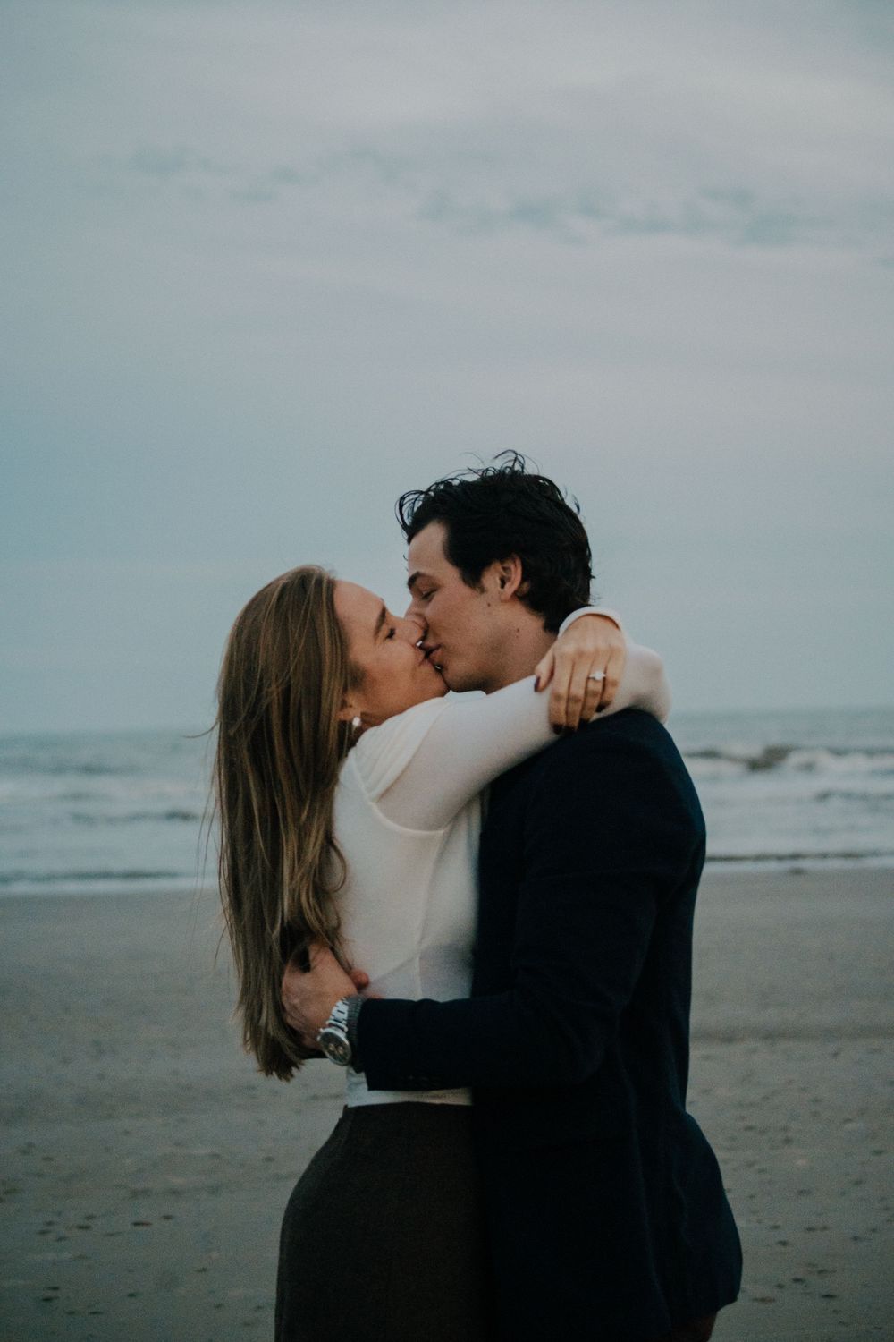 A couple shares an intimate moment on a cloudy beach, captured in a romantic sequence of photos.