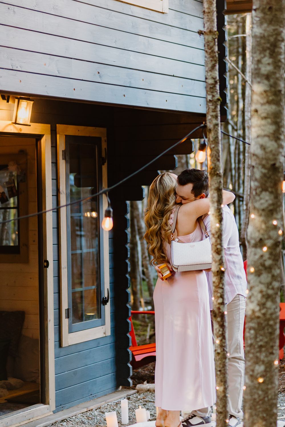 Romantic moment captured outside a blue cottage with string lights and a red swing in the background.
