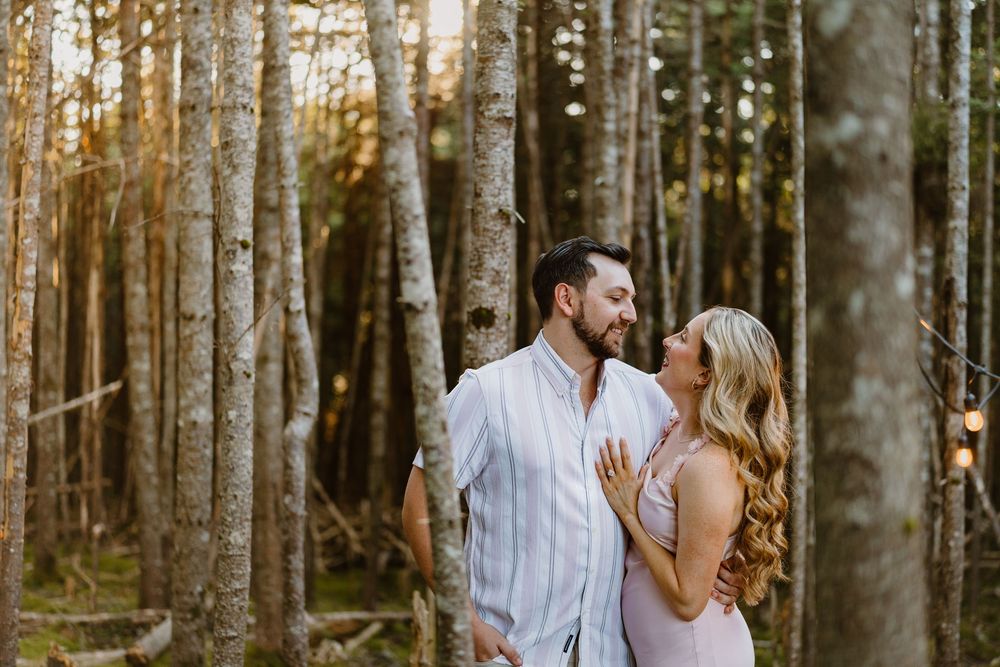 A couple shares a tender moment while embracing in a sun-dappled forest setting during a photo shoot.