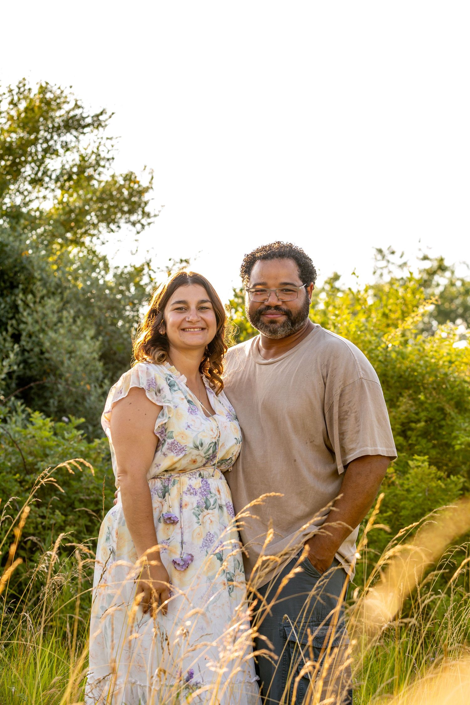 Couple sitting together in tall grass during golden hour.
