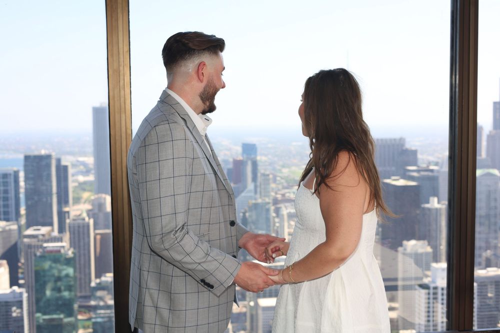 A couple shares a romantic moment overlooking a cityscape from a high-rise building window.