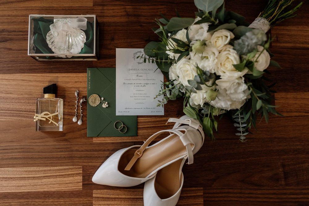 Wedding details including elegant white shoes, invitations and a lush white floral bouquet on wooden surface.
