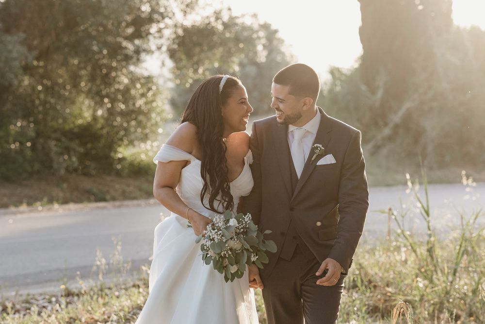 A bride and groom share a romantic moment in golden sunlight while holding a greenery bouquet.