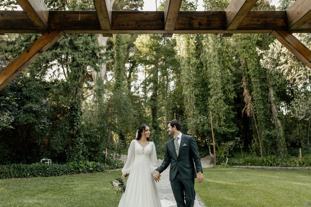 A romantic garden ceremony setting with greenery and wooden pergola overhead.