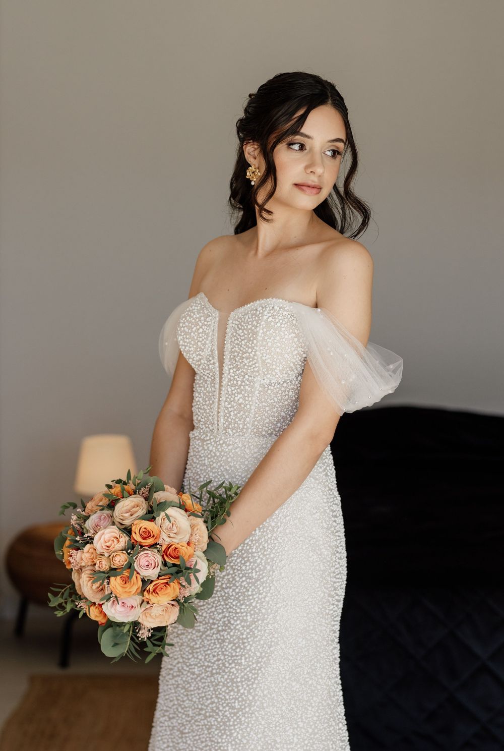Elegant bride in a beaded wedding dress holds a peach and coral bouquet.
