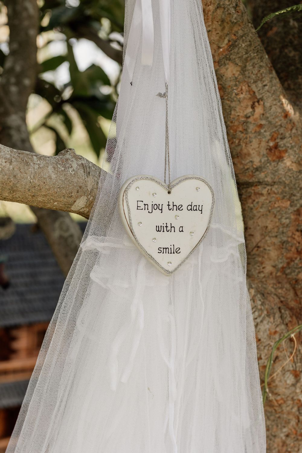 A heart-shaped sign reading 'Enjoy the day with a smile' hangs on white wedding veil fabric.