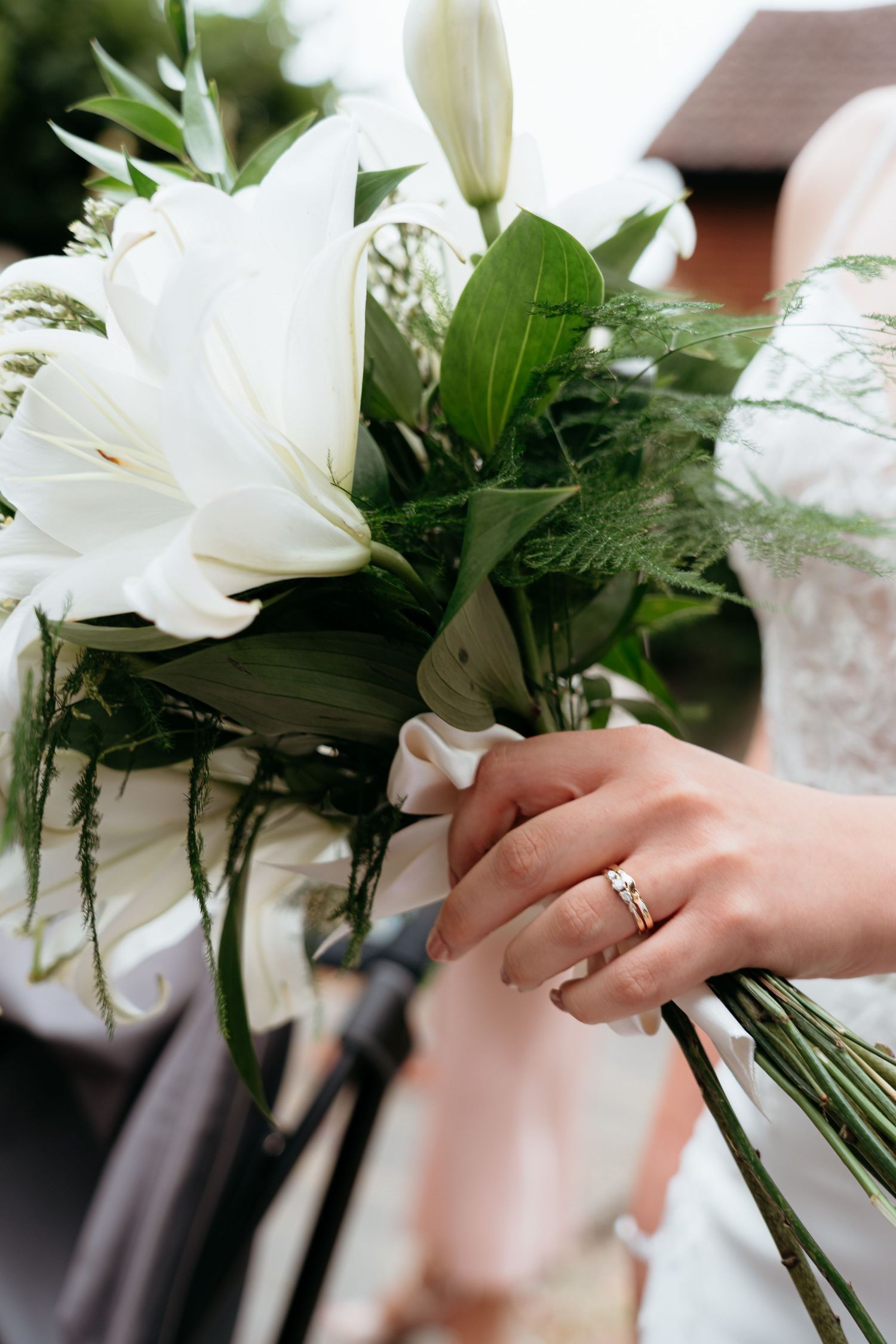 Close-up of hands holding white lily wedding bouquet with an engagement ring sparkling on the finger.