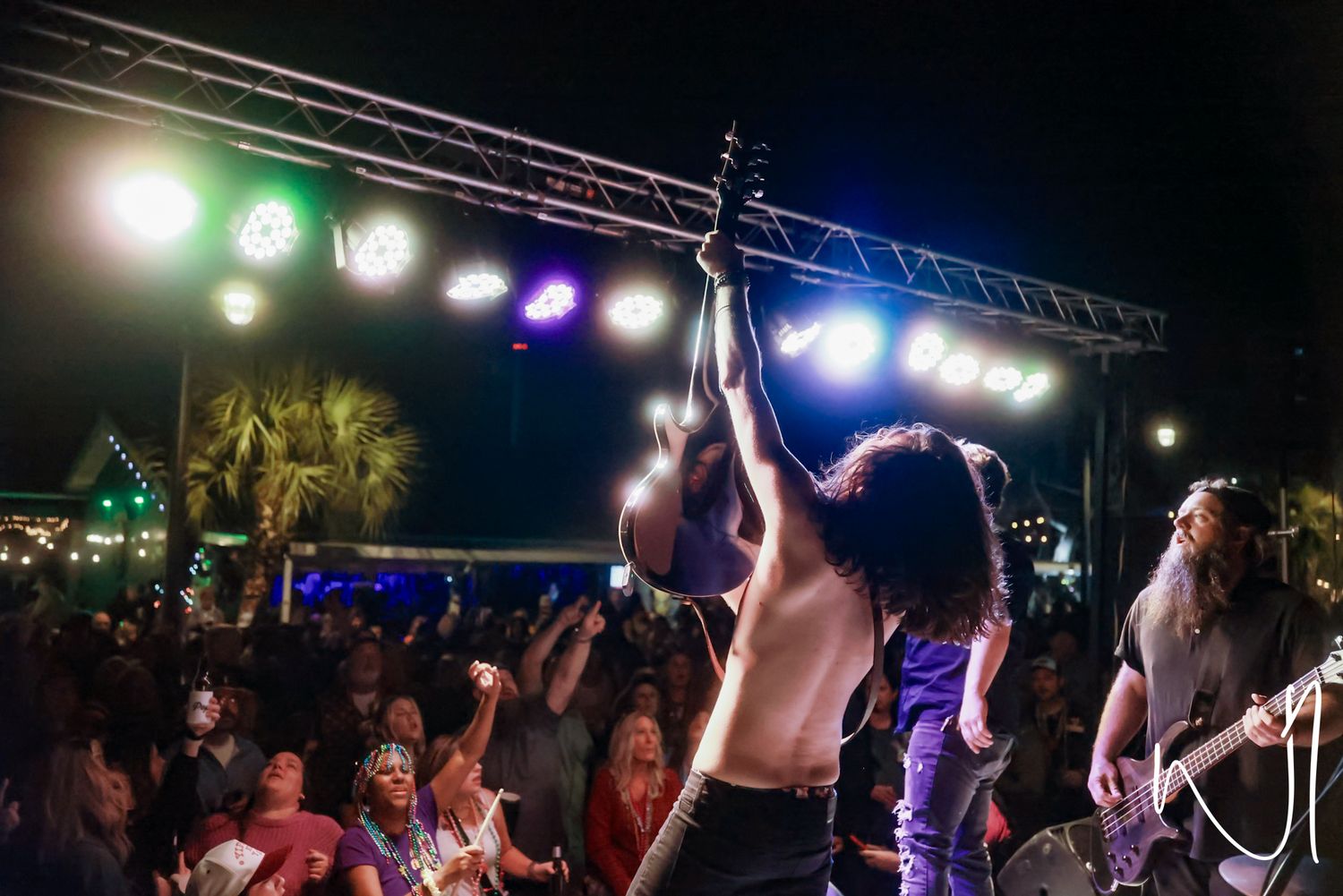 A performer on stage energetically holds up a microphone stand during an outdoor concert.