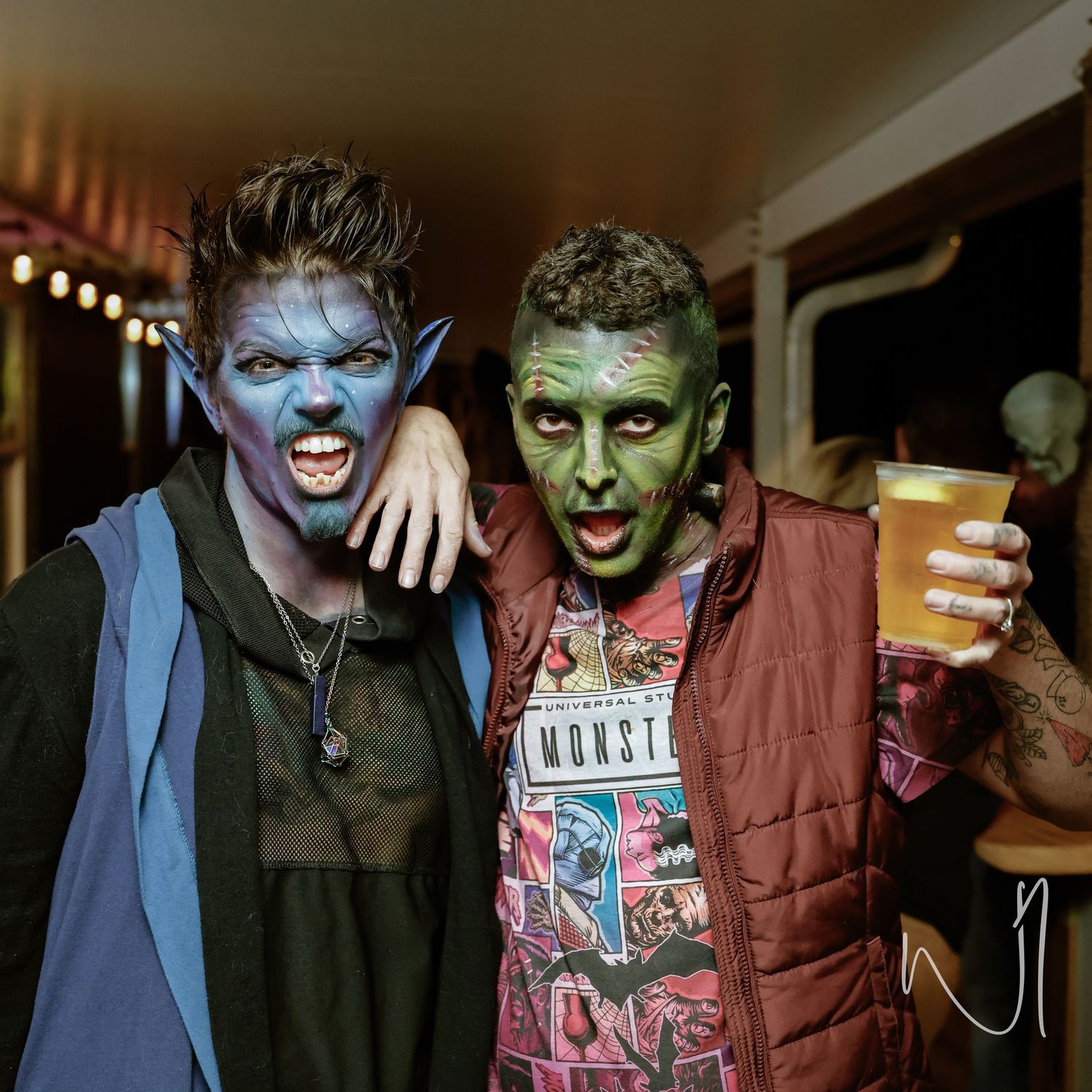 Two Halloween party attendees with face paint pose together with a beer.